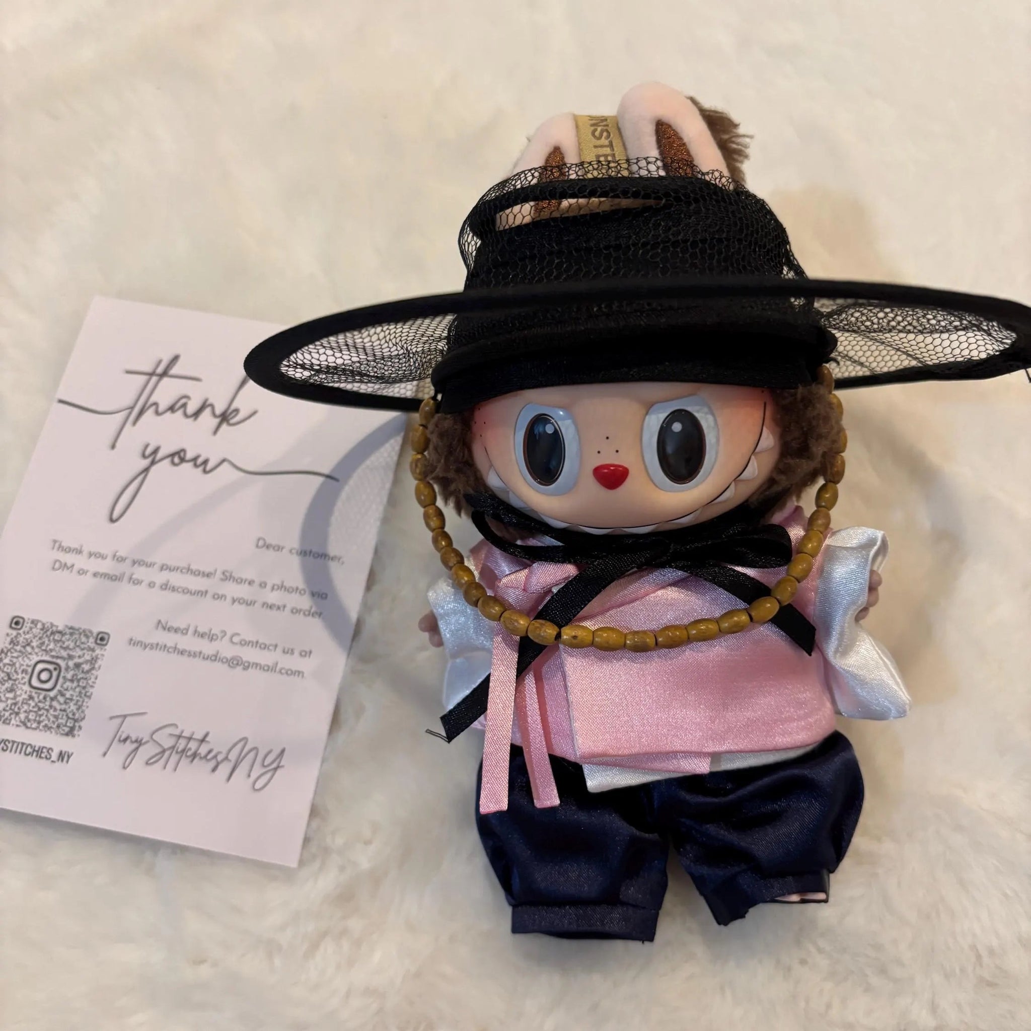 Small doll with a black hat and pink outfit on a light background